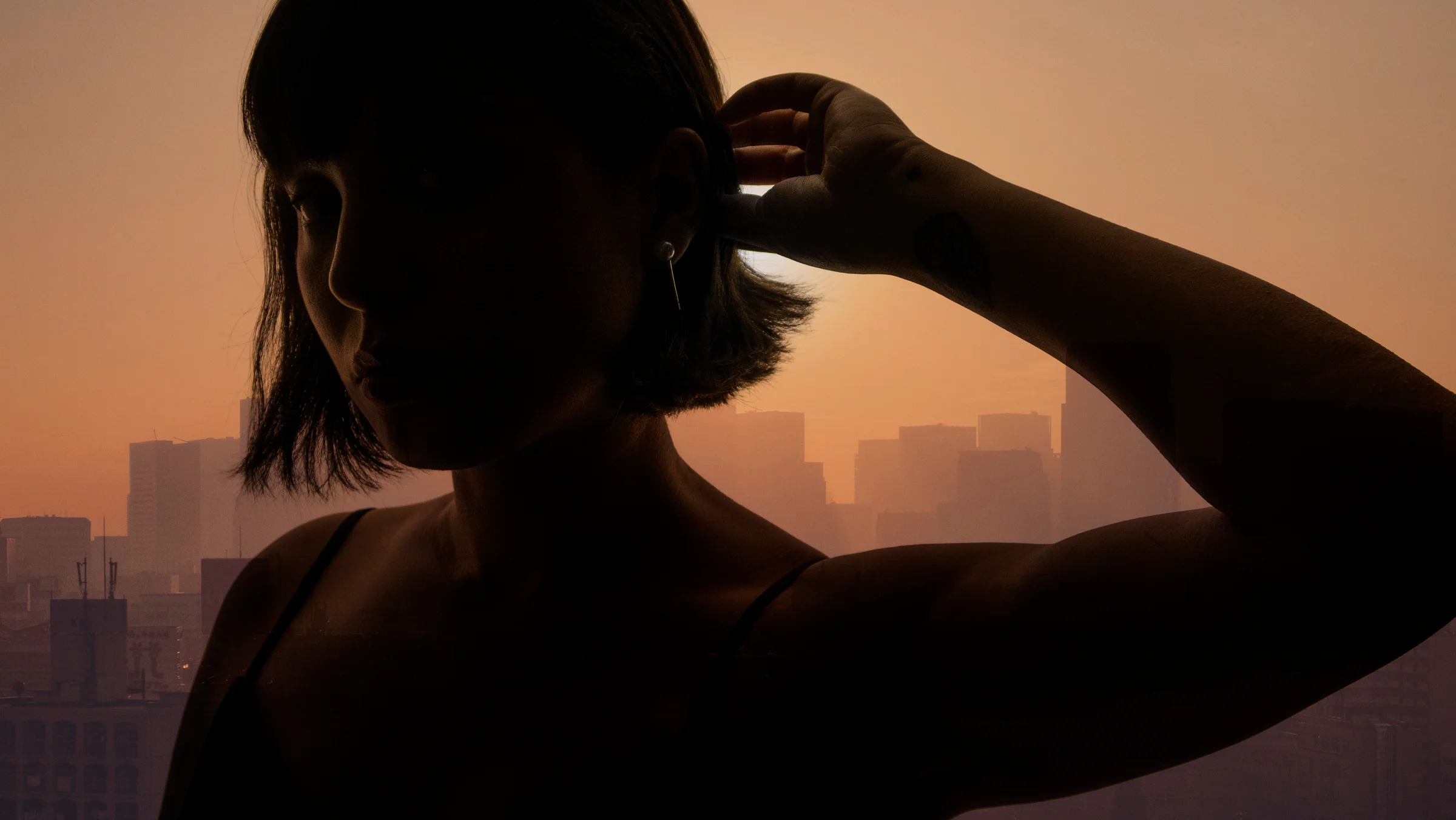 Double-exposure photograph of a woman with the Tokyo skyline in the background at sunset.